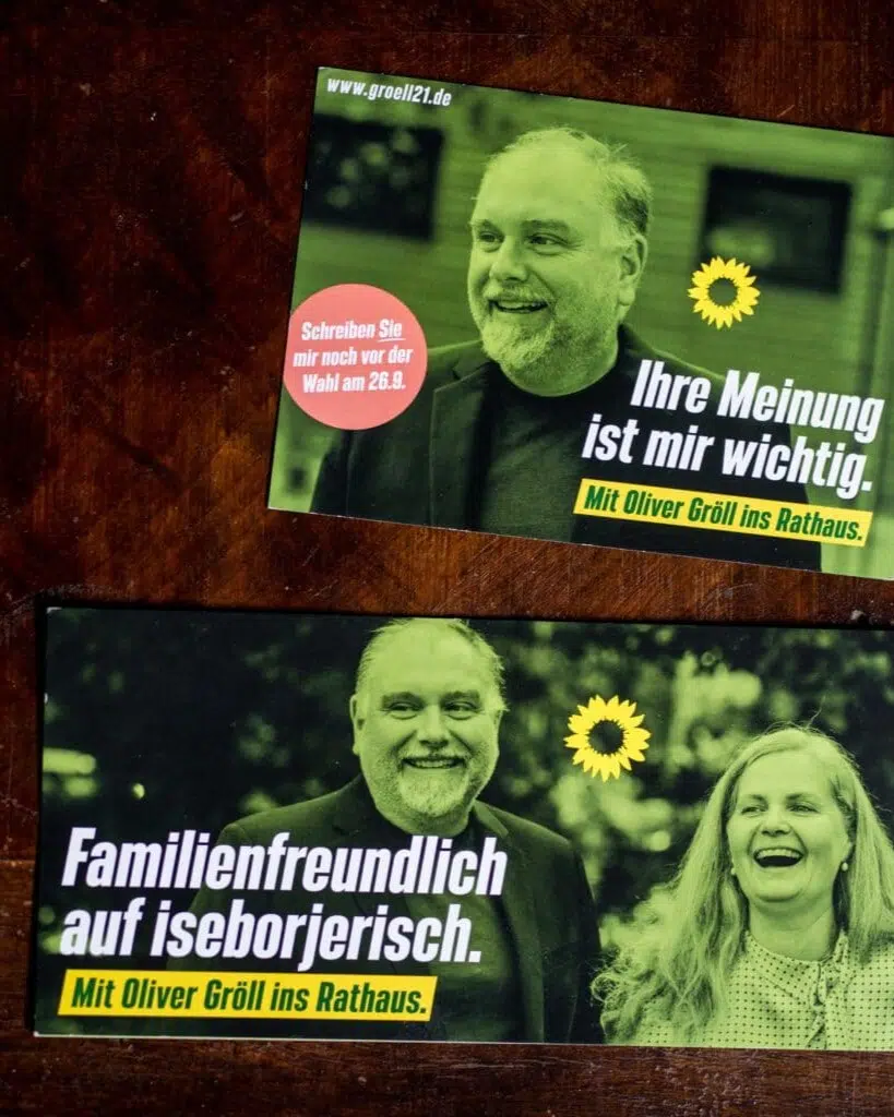 Auf einem Holztisch liegen zwei Postarten für die Wahl des Bürgermeisterkandidaten Oliver Gröll der Grünen in Neu-Isenburg